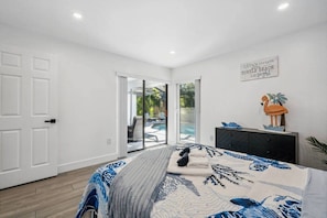 A bedroom with a bed, a dresser, a wall decoration, and a sliding glass door leading to a patio. - Florida Fun! Beach Theme, Heated Pool, Near Siesta (Sarasota)