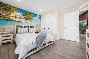 A bedroom with a bed, a nightstand, a wardrobe, and a mural of a beach scene. - Florida Fun! Beach Theme, Heated Pool, Near Siesta (Sarasota)