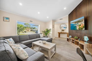 A modern living room with a grey sectional sofa, a wooden coffee table, and a TV mounted on a wooden wall.