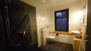 Un baño moderno con ducha de vidrio, inodoro y lavamanos con ventana arriba.