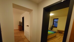 Una habitación con una cama, una mesita, una ventana y una puerta que da a otra estancia.