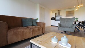 Un salon avec un canapé marron, un fauteuil gris et une table basse en bois sur laquelle sont posés deux vases blancs.