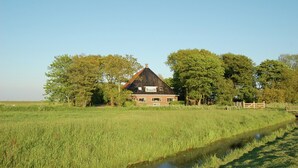 Une maison avec un toit en pente, entourée d’un champ et d’arbres.