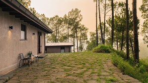 Un chalet rustique doté d’une terrasse en pierre, d’une petite table avec des chaises et offrant une vue sur de grands pins.