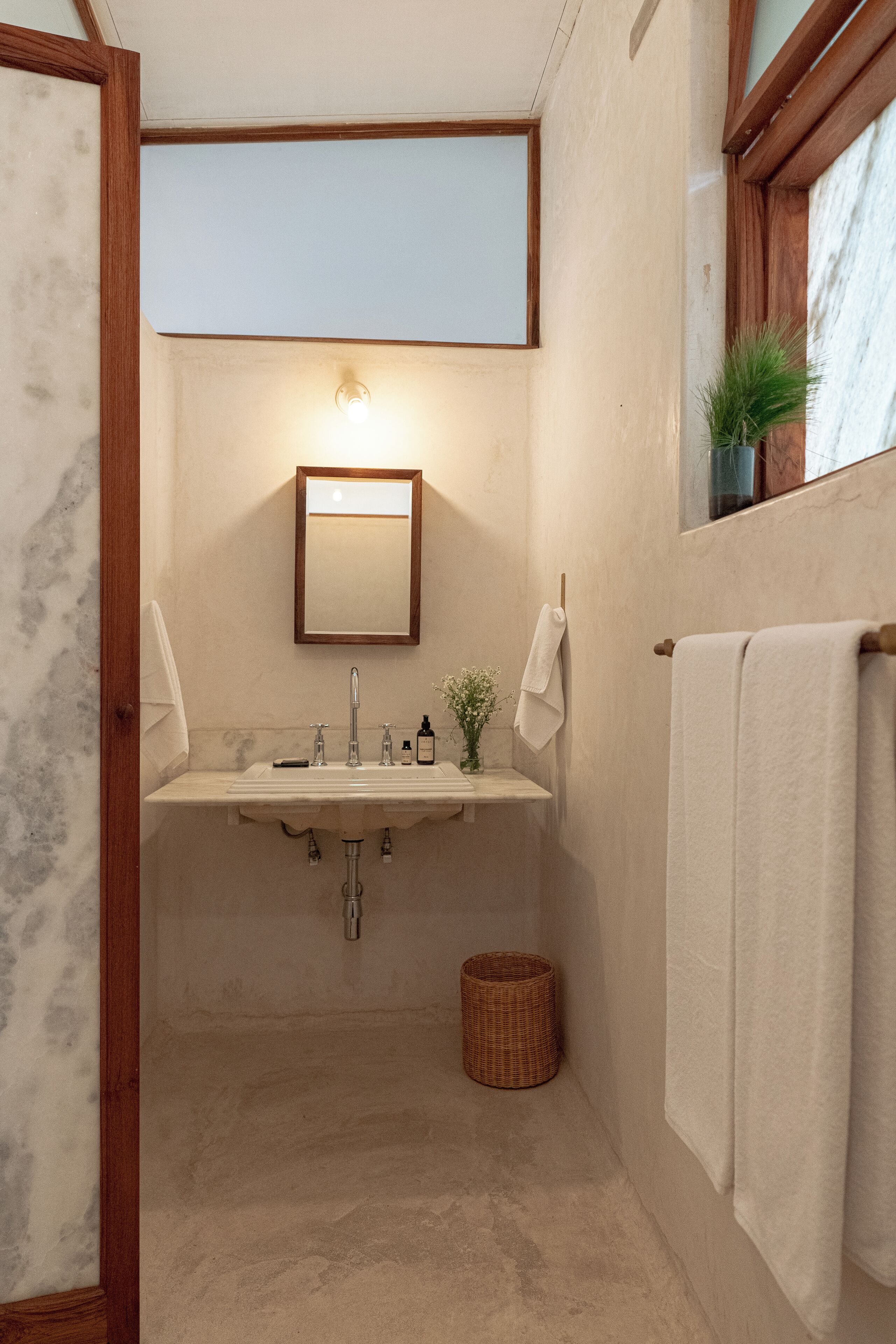 A bathroom with a marble wall, a wooden-framed mirror, a sink with a towel, and a small plant.
