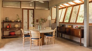 Un coin repas avec une table ronde, quatre chaises, un ventilateur de plafond et une vue dégagée grâce à de grandes fenêtres.