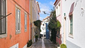 Une rue pavée bordée d’immeubles à l’architecture traditionnelle, un ciel dégagé et un étroit sentier.