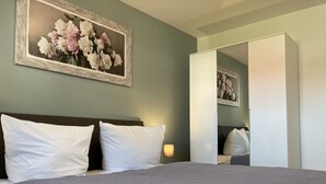 A neatly made bed with white pillows and a grey bedspread, a painting of flowers on the wall, and a wardrobe with a mirror. - The "Seebär" in Haus Meeresglück, close to the beach and central! - House Meeresglück (Dahme)