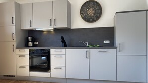 A modern kitchen with grey cabinets, a built-in oven, a coffee maker, and a wall clock. - The "Seebär" in Haus Meeresglück, close to the beach and central! - House Meeresglück (Dahme)
