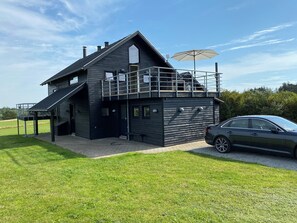 Ein modernes, zweistöckiges Haus mit Balkon, einem geparkten Auto davor und einem Rasen.