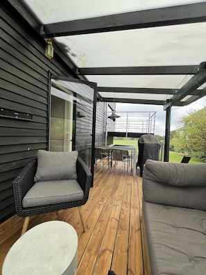Un patio exterior cubierto con piso de madera, muebles de mimbre y vista al jardín trasero.