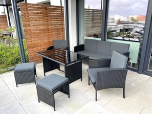 Un espace extérieur moderne, aménagé avec une table à plateau en verre, des chaises en osier et un banc rembourré.