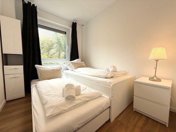 A bedroom with a bed, a nightstand, a lamp, a wardrobe, and a window with curtains.