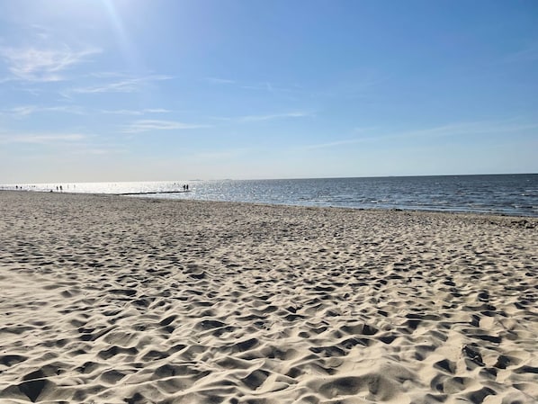 Une plage de sable fin, avec un ciel dégagé et une mer calme.