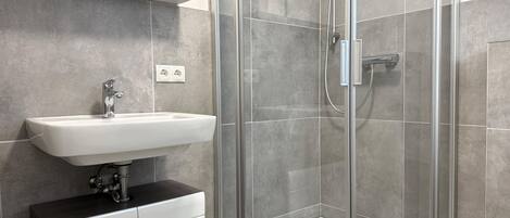 A modern bathroom with a glass-enclosed shower, a white sink, and a mirror above the sink.