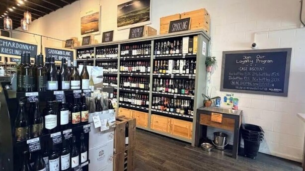 Une cave à vin avec des étagères remplies de différents vins, un panneau indiquant un programme de fidélité et un menu écrit à la craie.