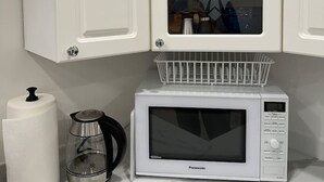 Une cuisine avec des meubles blancs, un four à micro-ondes, une machine à café et un rouleau d’essuie-tout.