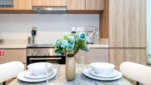 A modern kitchen with a gas stove, wooden cabinets, and a vase with artificial flowers on the counter. - Modern Studio Living at Missoni (Dubai)