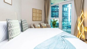 A hotel room with a large bed, a view of the city through a glass door, and a decorative wall piece. - Modern Studio Living at Missoni (Dubai)