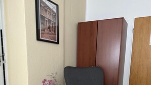A room with a grey armchair, a small wooden side table with a vase of flowers, a framed picture on the wall, and a wardrobe. - Hotel Süden (Berlin)