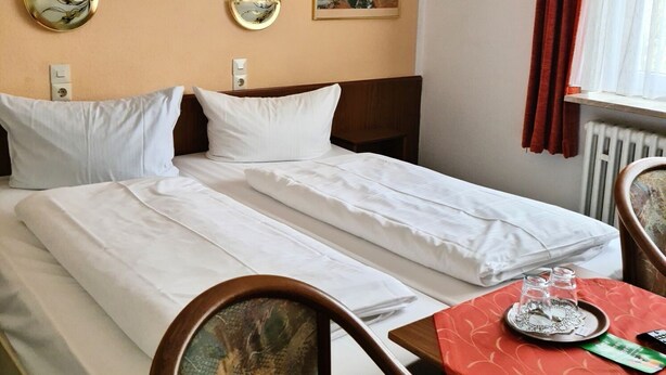 A double bed with white linens, two bedside tables, a small table with a tray, and a painting on the wall. - Hotel Süden (Berlin)