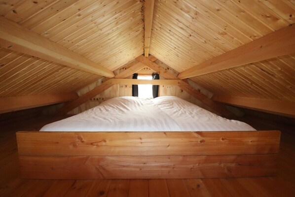 A wooden loft bedroom with a sloped ceiling, a central window, and a bed with white bedding. - Cottages in Friesland with Farm Experience (Tjerkgaast)