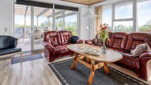 Una sala de estar moderna con un sofá de cuero, una mesa de centro de madera y vistas al exterior a través de amplios ventanales.