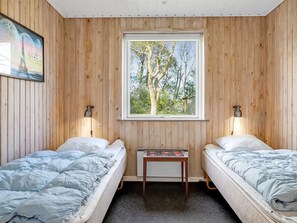 Ett rum med två sängar, träväggar, ett fönster med utsikt över träd och ett litet bord.