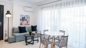 Un salon moderne avec un canapé, une table basse et une table à manger avec des chaises. On peut y voir un tableau au mur, une lampe sur pied et un appareil de climatisation.