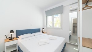 A modern bedroom with a large bed, bedside tables with lamps, a window with a view, and a mirror.
