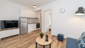 A modern kitchen with white cabinets, a built-in oven, and a TV on a wooden counter.