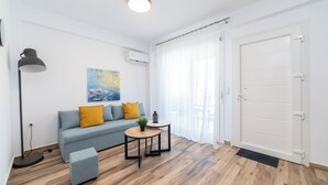 A modern living room with a grey sofa, mustard cushions, a small round table with a plant, a floor lamp, and a large white door.