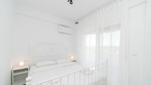 Une chambre à coucher blanche, avec un lit, des tables de chevet et un appareil de climatisation.