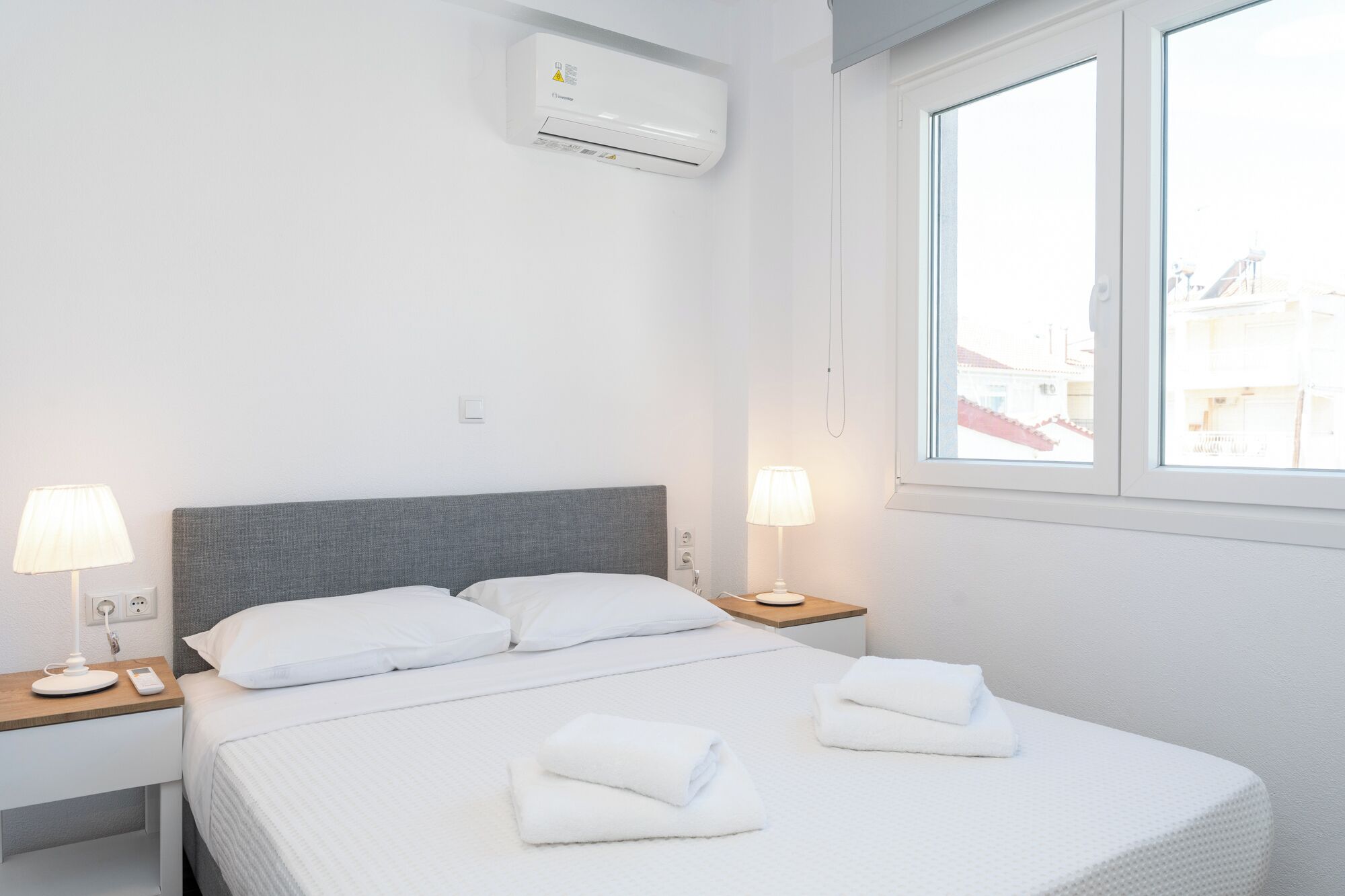 Et hotelværelse med seng, to sengeborde, et vindue og en aircondition.