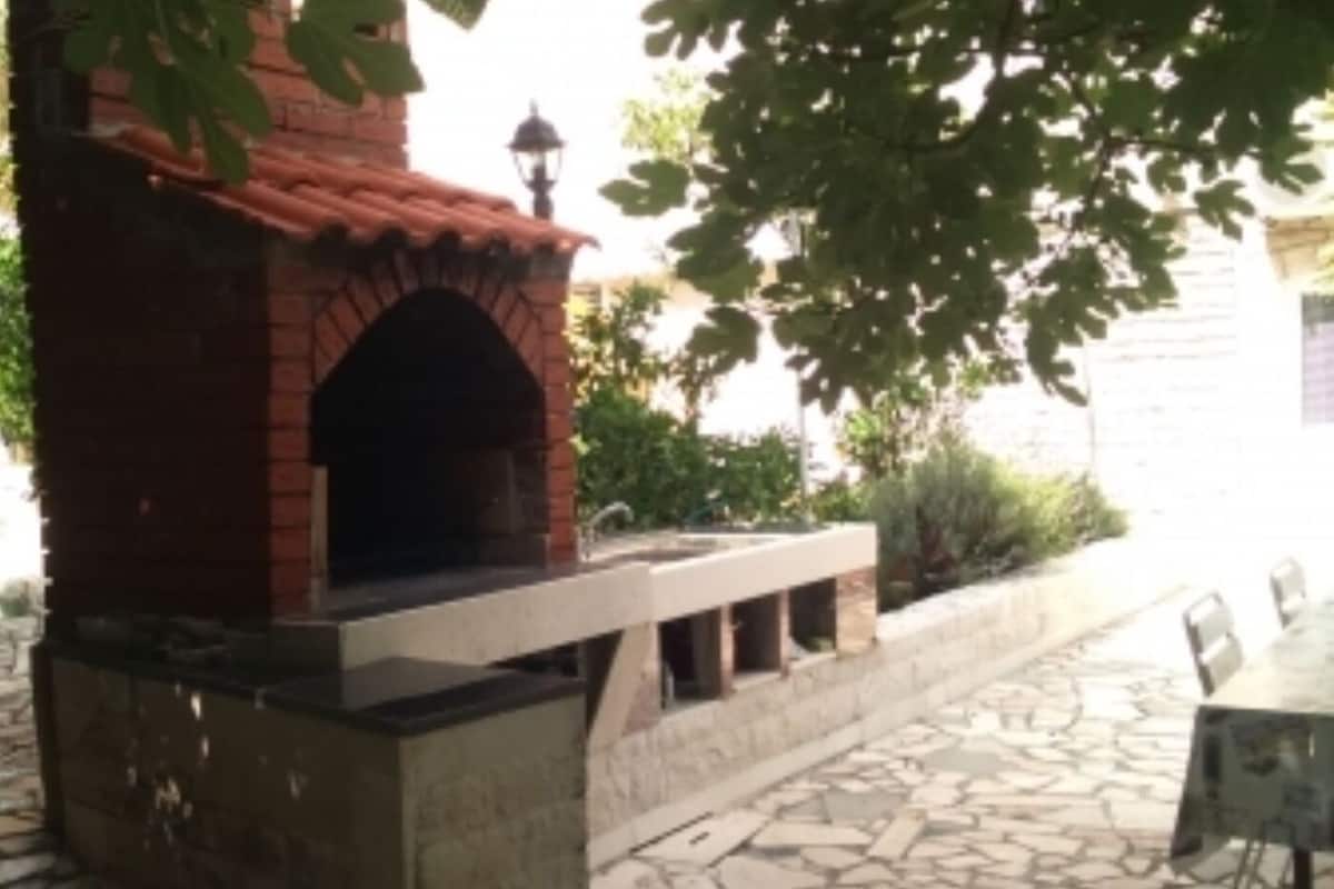 A brick outdoor oven with a stone base, surrounded by greenery and a tiled patio area.