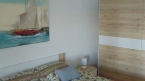 Une chambre à coucher comprenant un lit, une table de chevet, une lampe, une armoire en bois et un tableau représentant un voilier accroché au mur.