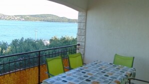 Un balcon avec une table et des chaises, donnant sur une étendue d’eau et sur de la verdure.