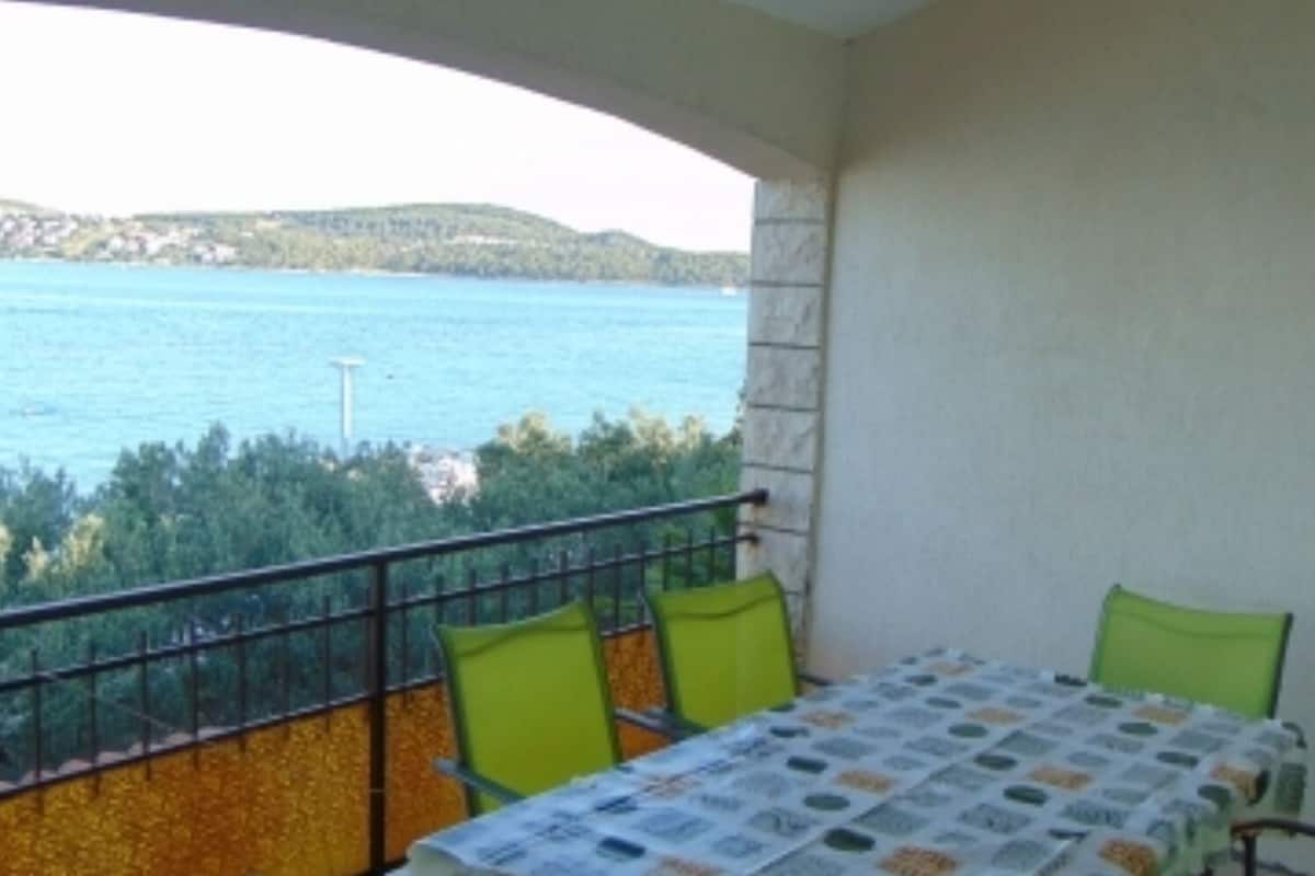 A balcony with a table and chairs, overlooking a body of water and greenery.