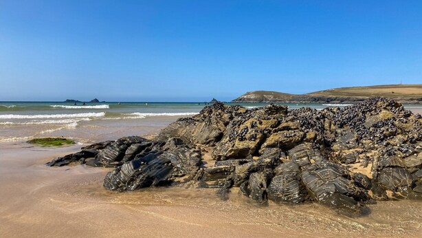 A rocky beach with waves, a clear sky, and distant hills. - Cottage in Cornwall near Sandy Beach (Rock)