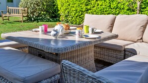 A wicker outdoor seating area with cushions, a table set with plates, cups, and a teapot. - Cottage in Cornwall near Sandy Beach (Rock)