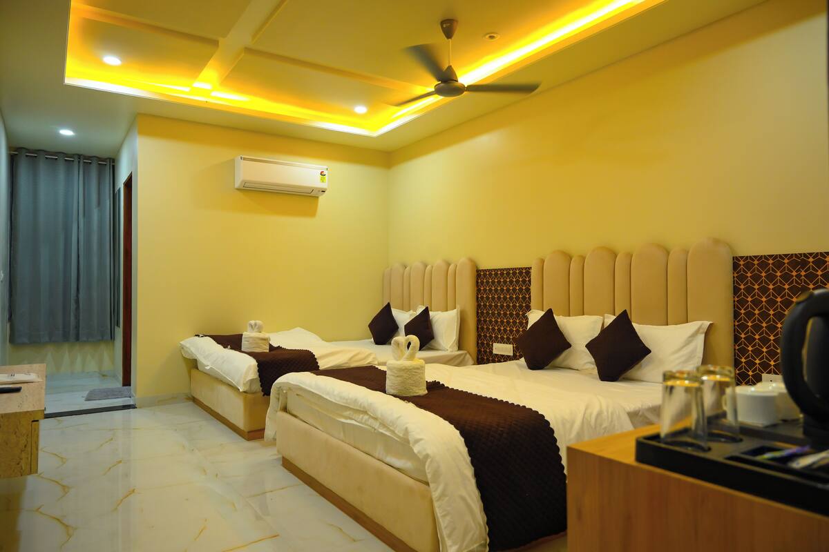 A hotel room with two beds, a ceiling fan, an air conditioning unit, and a desk with a telephone and a cup.