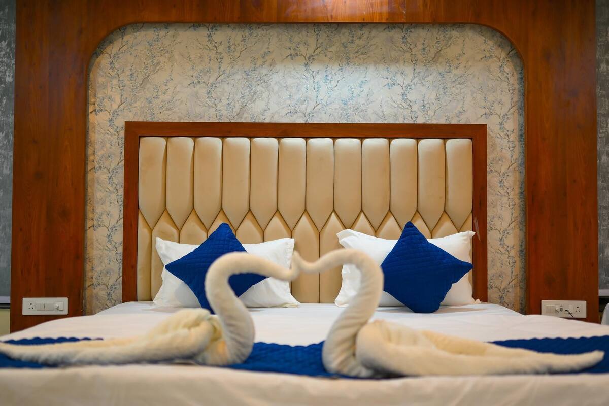 A bed with a tufted headboard, white and blue pillows, and two swans made of towels.