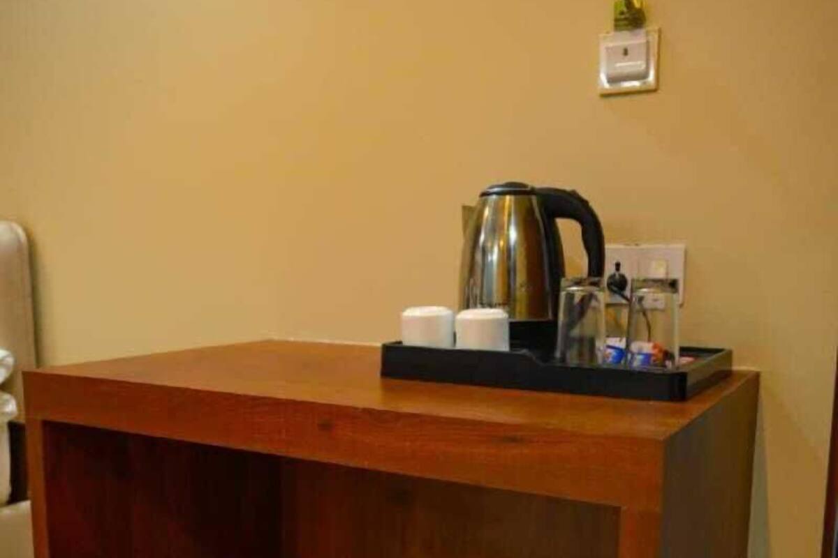 A wooden table with a kettle and cups, a power outlet, and a small plant on the wall.