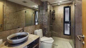 Un baño moderno con un espejo grande, un lavamanos sobre encimera, una ducha con mampara de vidrio y un inodoro.