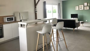 A modern kitchen with white cabinetry, a microwave, and a coffee maker. There is a dining area with a white table and chairs, and a TV on a stand.