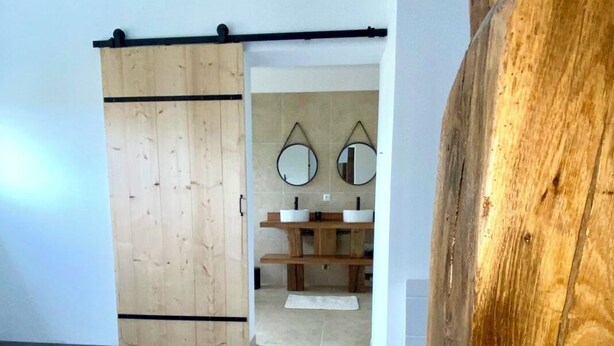 A room with a wooden sliding door, a small sink area with two mirrors, and a wooden bench.