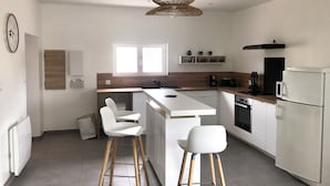 A modern kitchen with white cabinetry, a central island, wooden stools, a microwave, a coffee maker, and a built-in oven.