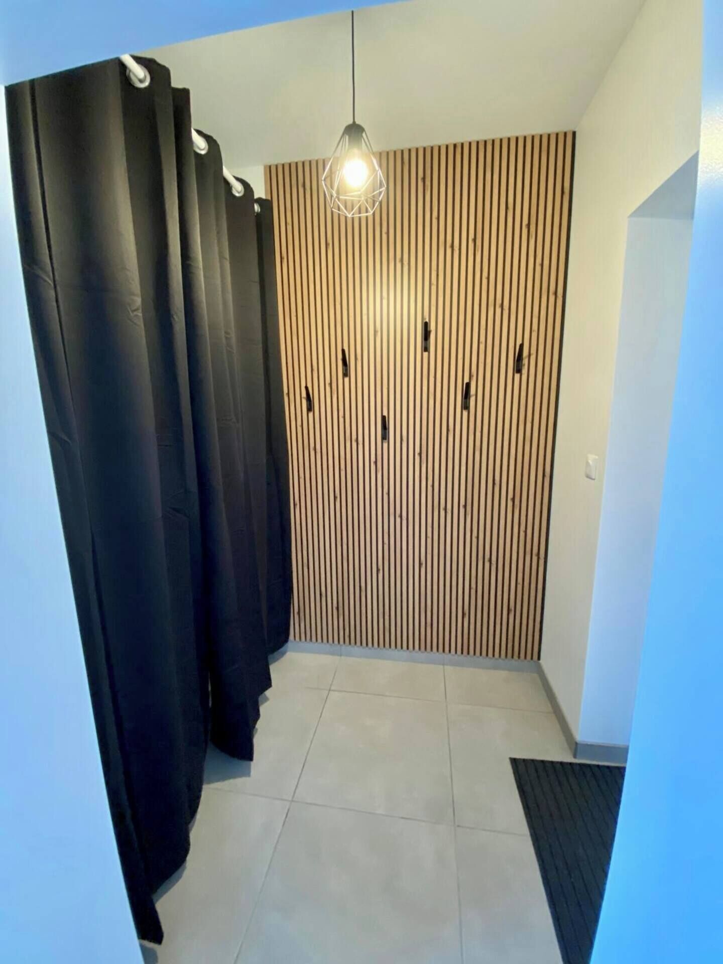 Ein modernes Zimmer mit einer Wand aus Holzleisten, einem schwarzen Vorhang und einer hängenden Leuchte.