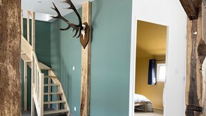A spacious interior with a staircase, a mounted deer head, and a bed in the adjacent room.
