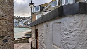 A narrow cobblestone street with a stone wall on one side and a building with a white exterior and a black roof on the other. - Apartment in St Ives near Porthminster Beach (St Ives)